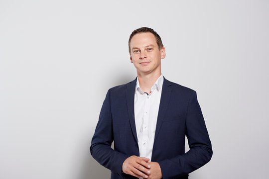 Mann in schwarzem Anzug und weißem Hemd vor hellgrauem Hintergrund