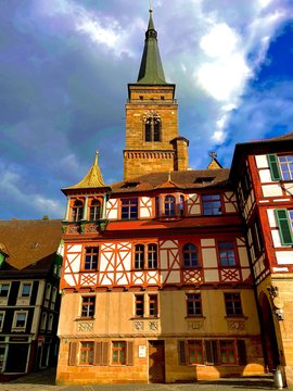 Rot-weisses Fachwerkhaus mit goldener Dachverzierung mit Kirchturmspitze im Hintergrund