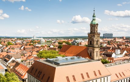 Ausblick auf eine Kirchturmspitze und die zumeist roten Dächer in Erlangen